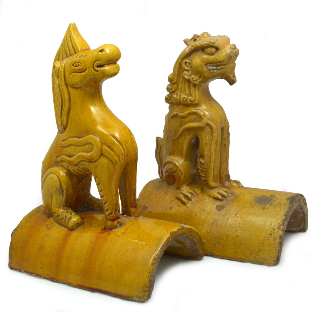 Two ridge tiles of semicircular section, glazed in Imperial yellow, surmounted by stylised animal figures sat on their haunches, one a horse and the other a Chinese guardian lion.